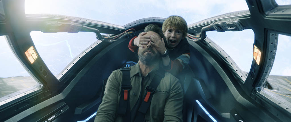 The older Adam and younger Adam in the cockpit at a dramatic yet comical moment during a chase sequence with Sorian’s jet pursuing them.