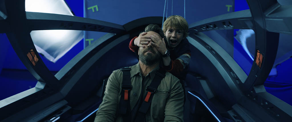 The older Adam and younger Adam in the cockpit at a dramatic yet comical moment during a chase sequence with Sorian’s jet pursuing them.