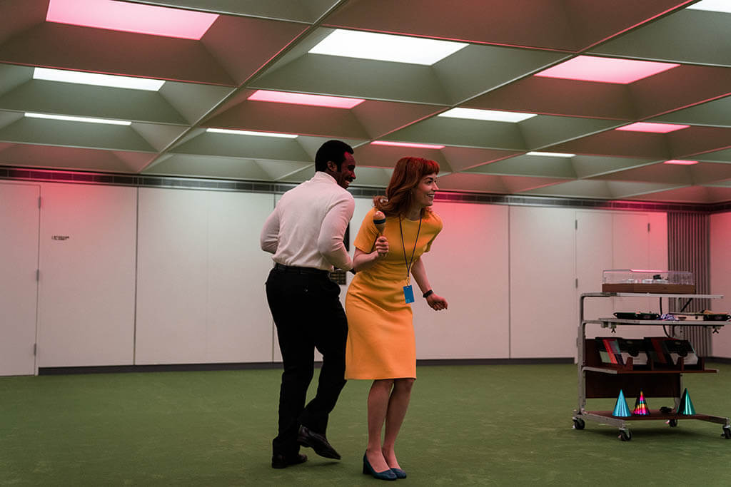 One of the silly incentives that workers receive at Lumon are “waffle parties.” Helly and Seth party in a sterile, symmetrical office, on a dance floor of green carpet.