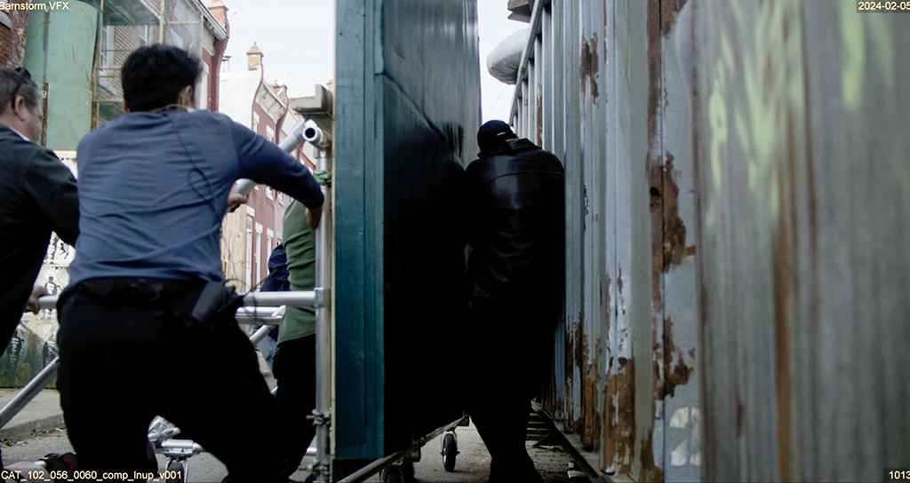 Grips compress a flat board against the actor to make look like he is being pushed against the dumpster by the CG truck. 